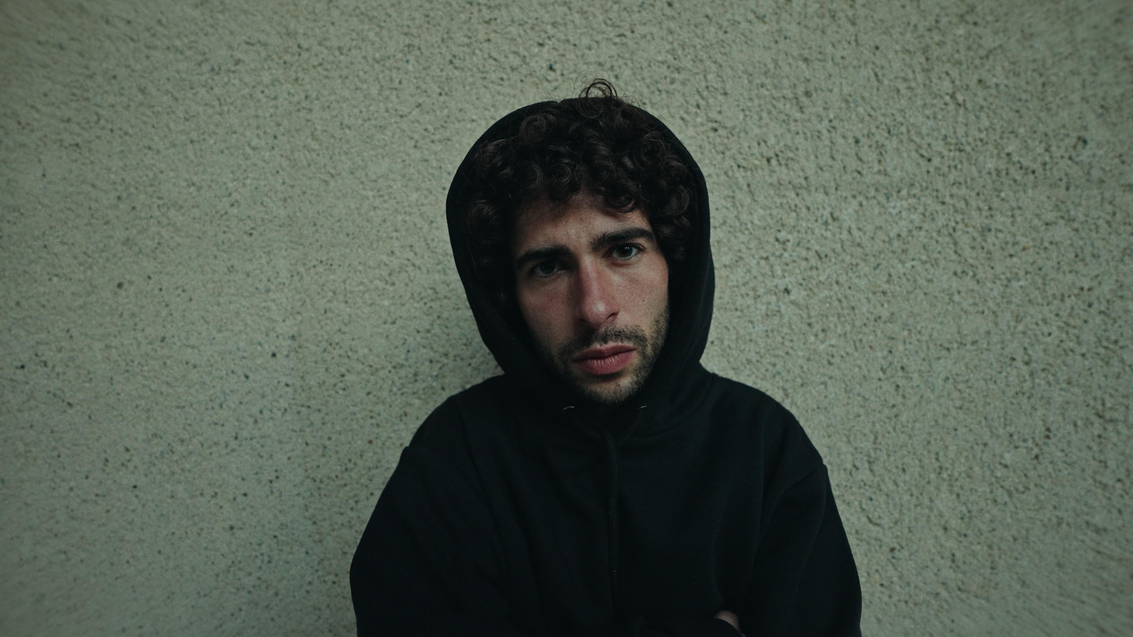 A dancer in a black hoodie seated against a stone wall.